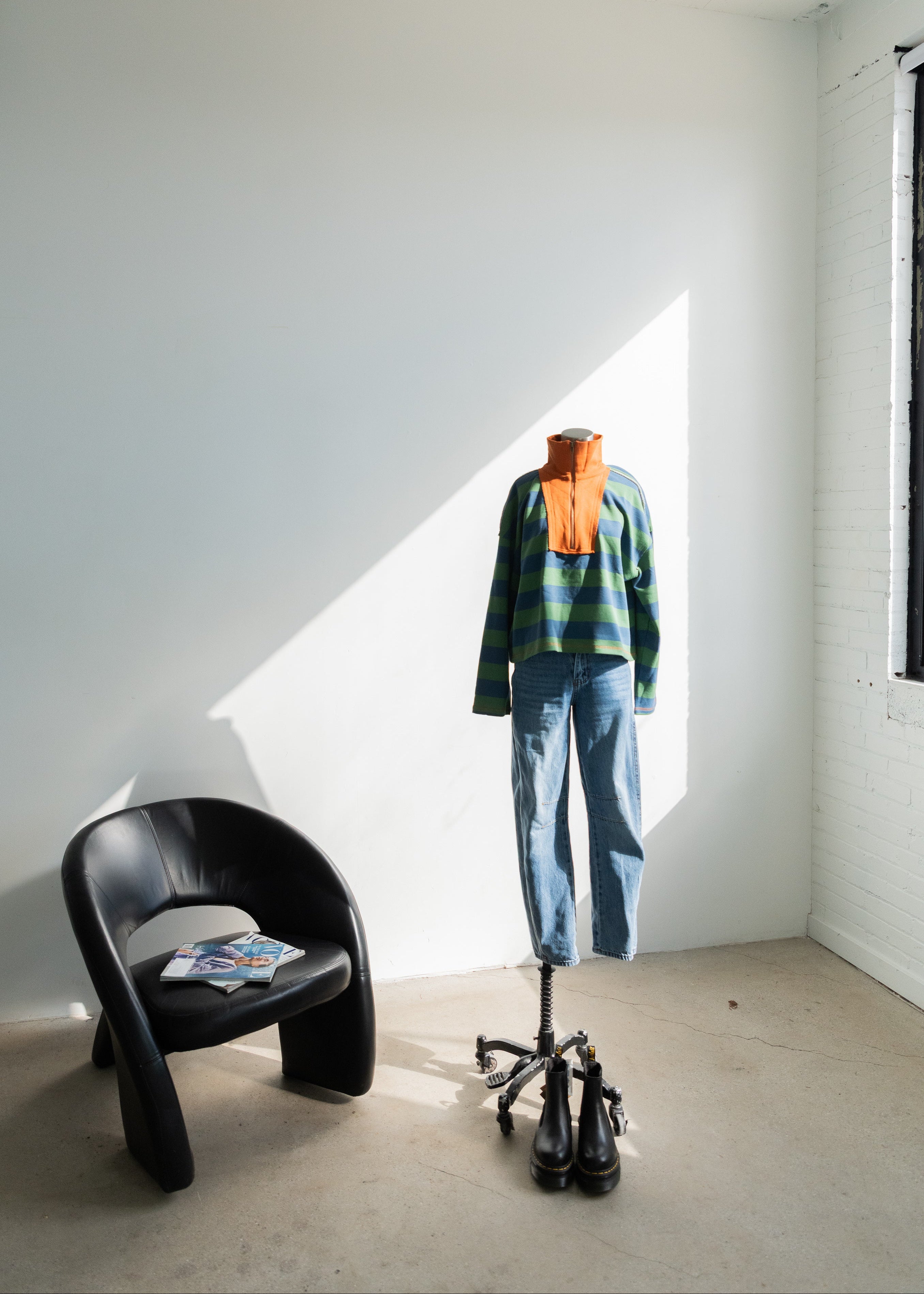 Mannequin wearing a striped sweater and jeans in a room with a black chair and open window.